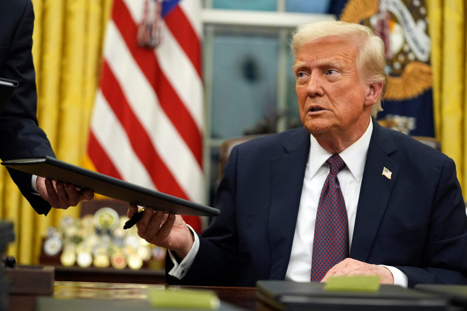 FILE - President Donald Trump signs executive orders in the Oval Office of the White House, Jan. 20...
