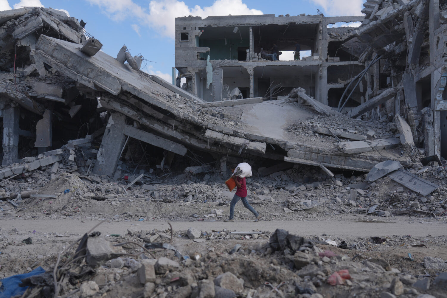 A Palestinian carries belongings while walking past destroyed buildings in Gaza City, Sunday, Oct. ...