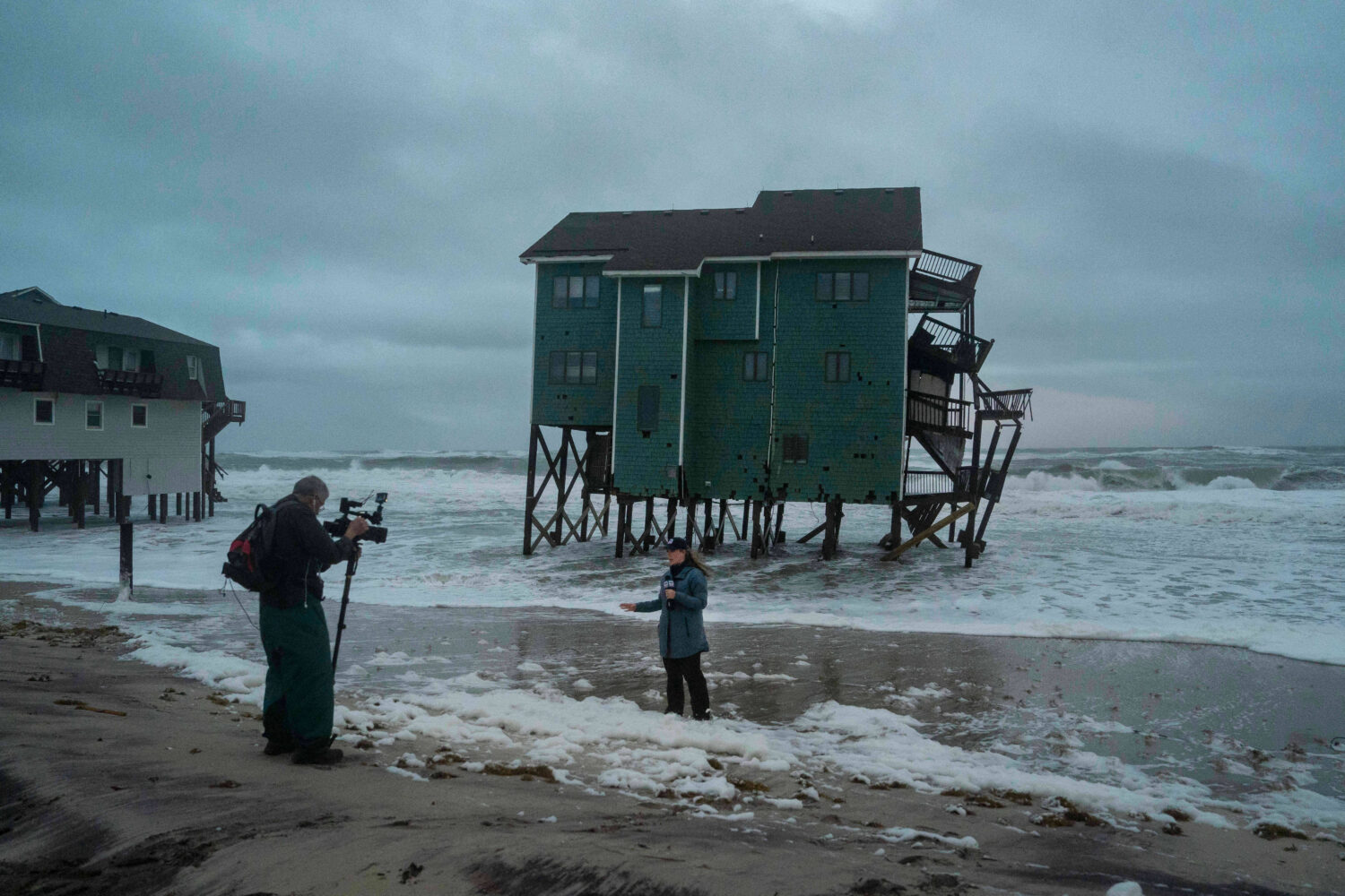 A Fox Weather reporter films in front of a house at risk of collapse in the midst of a storm, Sunda...