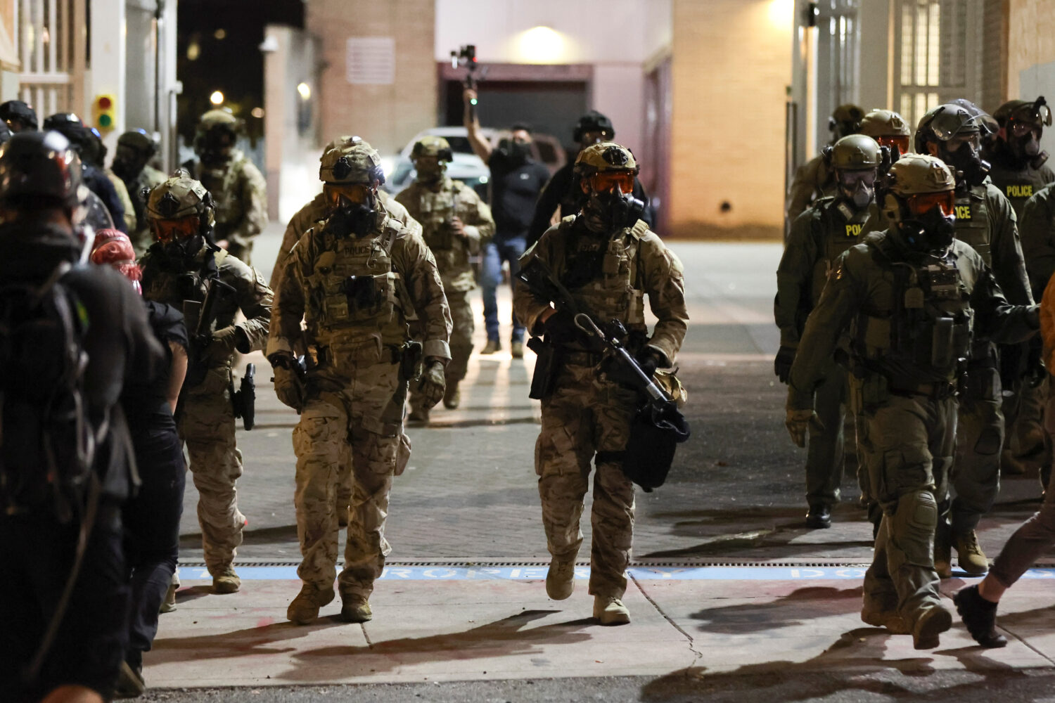 Federal agents walk into the street as people protest outside a U.S. Immigration and Customs Enforc...