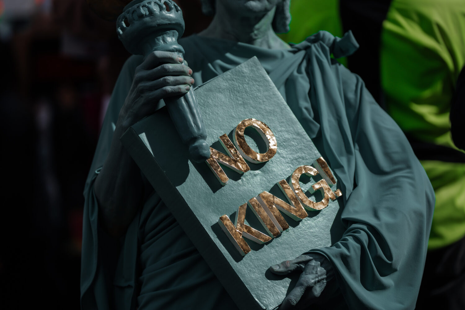 A Protester dressed in a Statue of Liberty costume holds a "No Kings" sign during a "No Kings" prot...