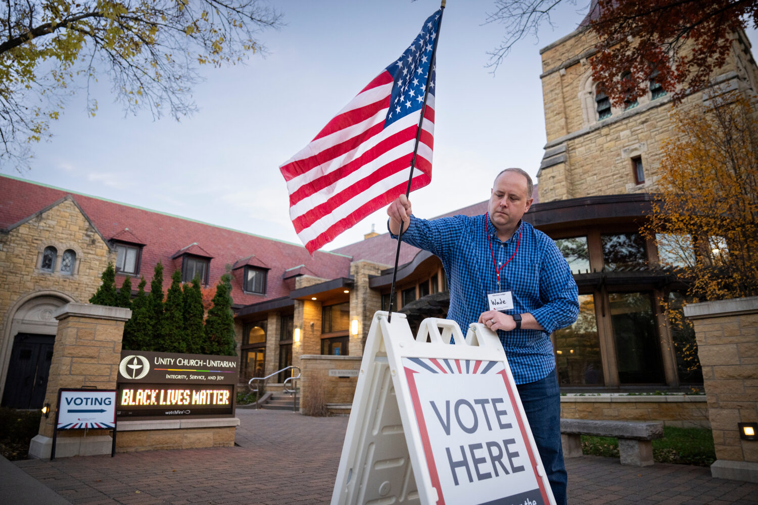 Wade Gustafson, a volunteer election judge, puts out the American flag and voting signs outside the...