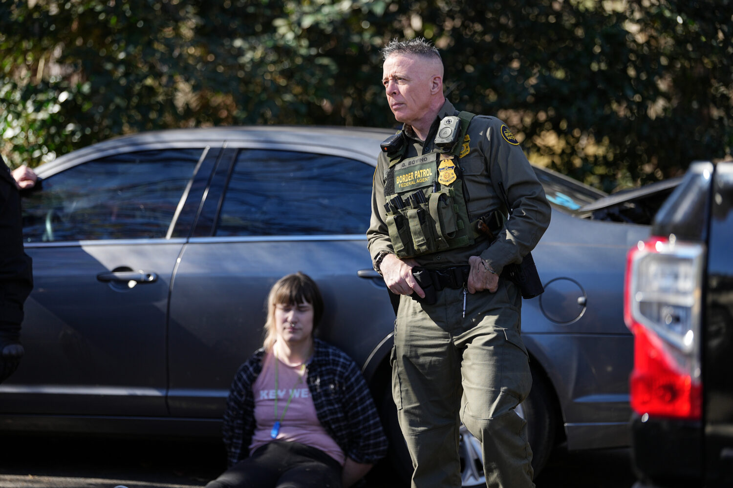 U.S. Border Patrol Commander at large Gregory Bovino, right, looks on as a detainee sits by a car, ...