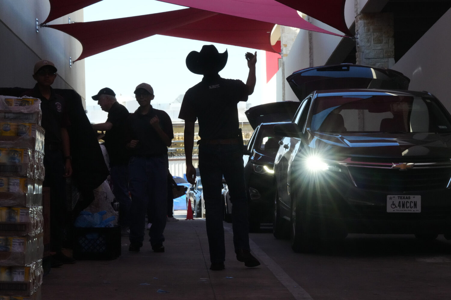 Aidan Tavor, center, directs traffic as volunteers help load vehicles during a food distribution at...