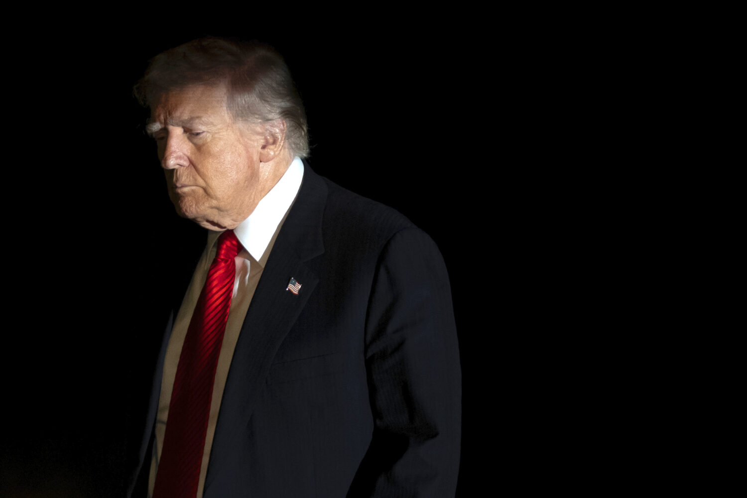 President Donald Trump is illuminated by a camera flash as he walks across the South Lawn of the Wh...