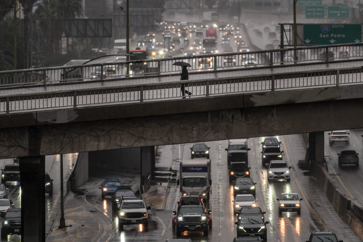 A pedestrian with an umbrella walks on a bridge over the rain-soaked 110 Freeway in Los Angeles Fri...