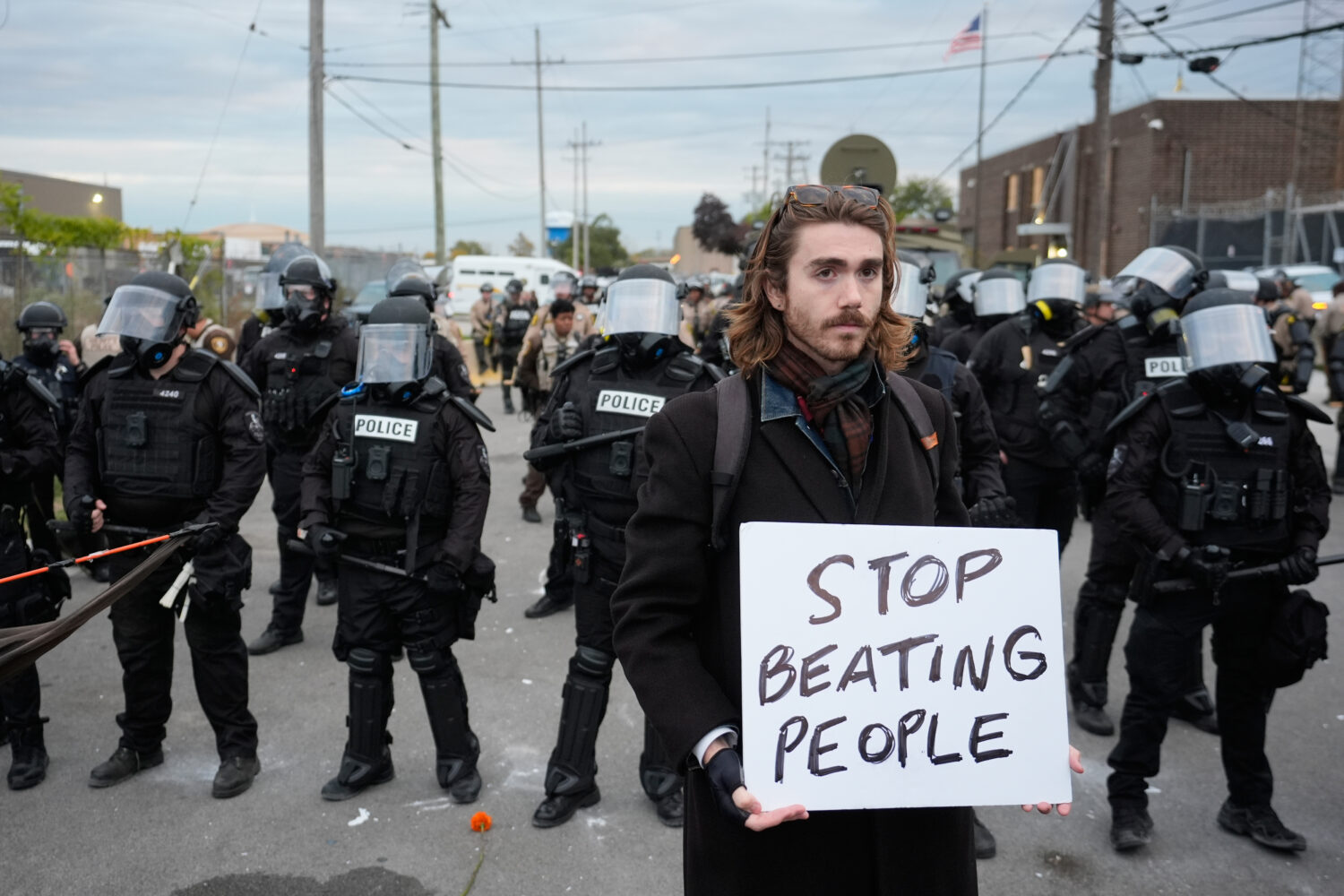 A demonstrator holds a sign reading "STOP BEATING PEOPLE" near a line of law enforcement as protest...