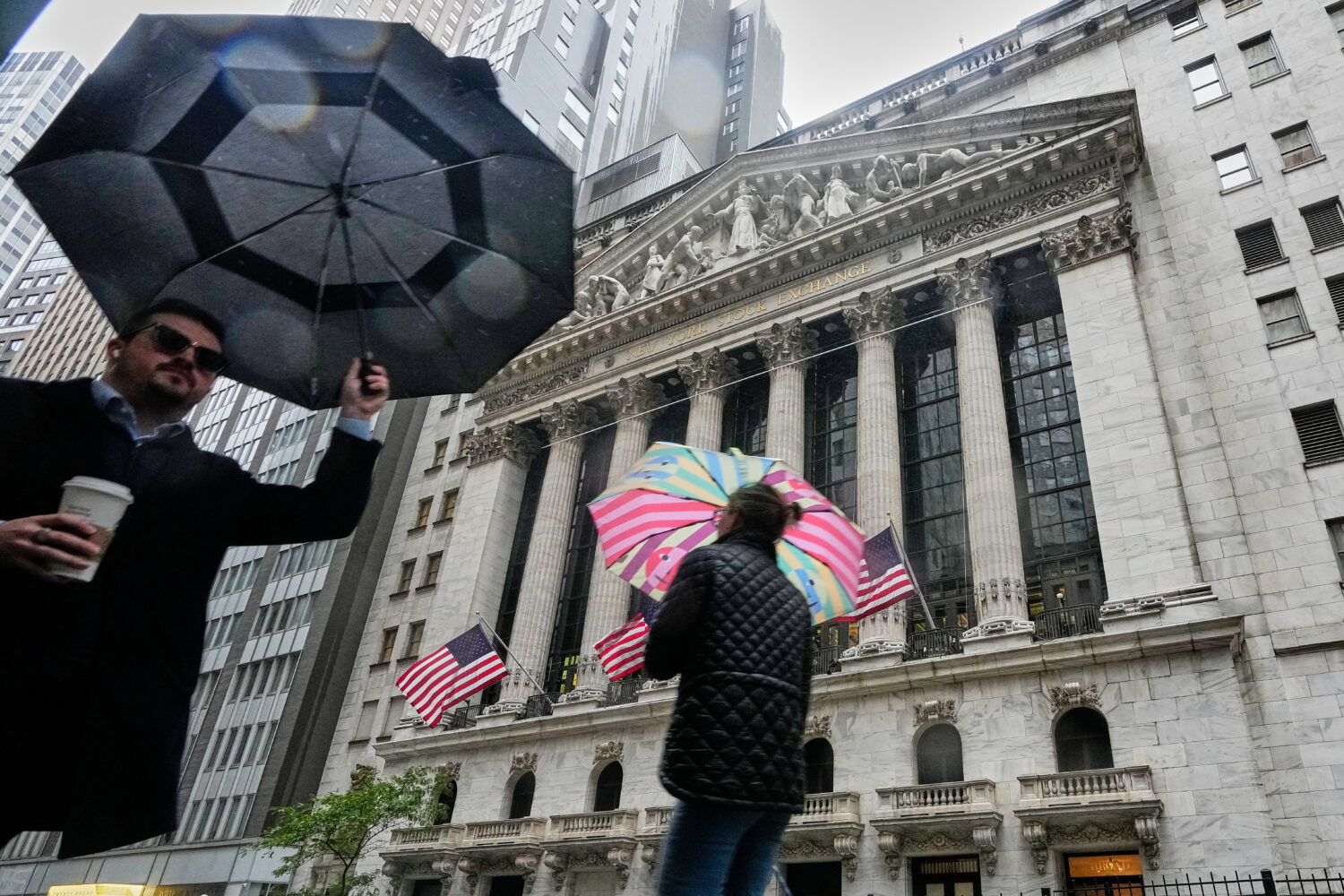 People with umbrellas pass the New York Stock Exchange, Monday, Oct. 13, 2025. (AP Photo/Richard Dr...
