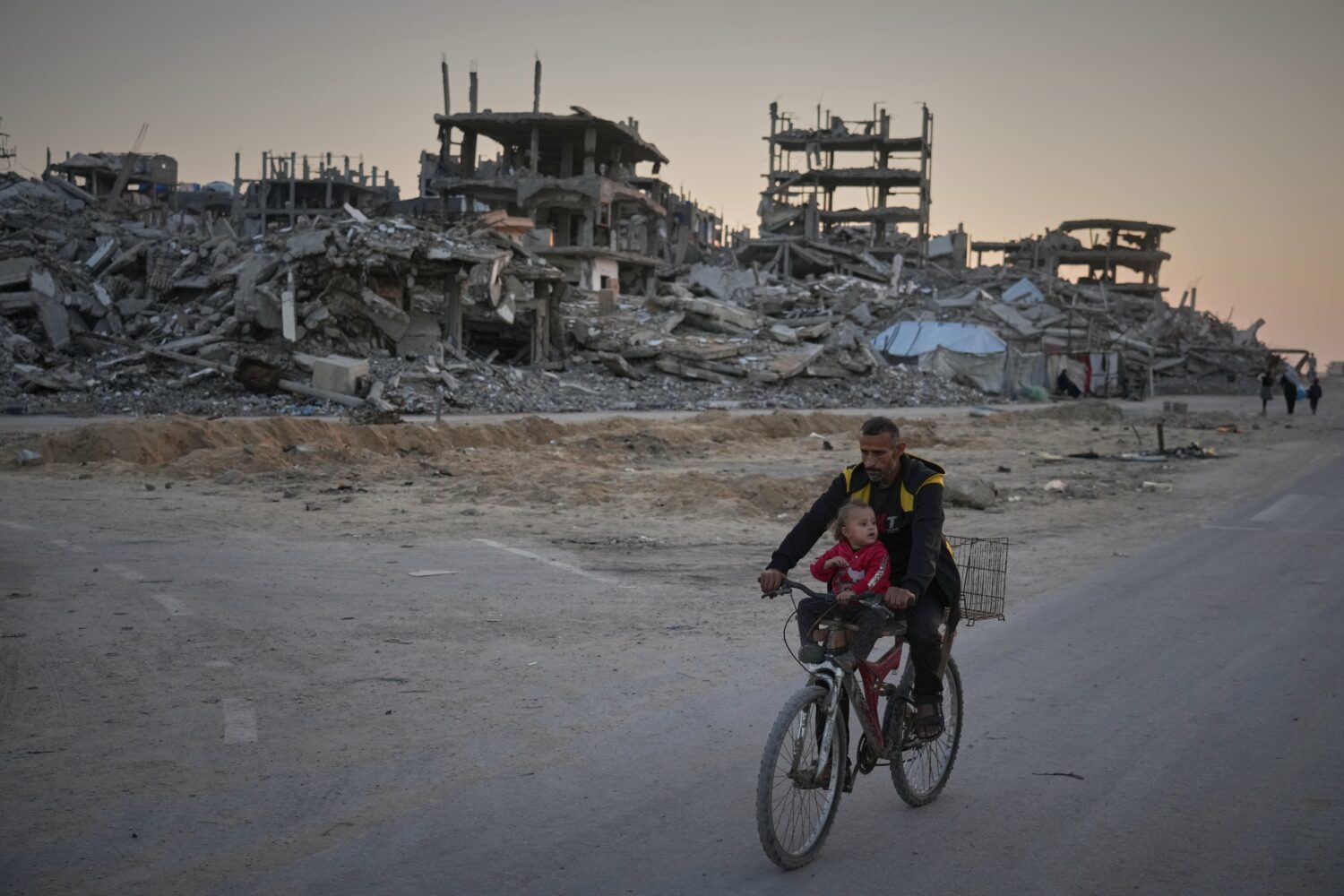 A man carries a child while riding his bicycle along a damaged street in the Al-Shati camp in Gaza ...