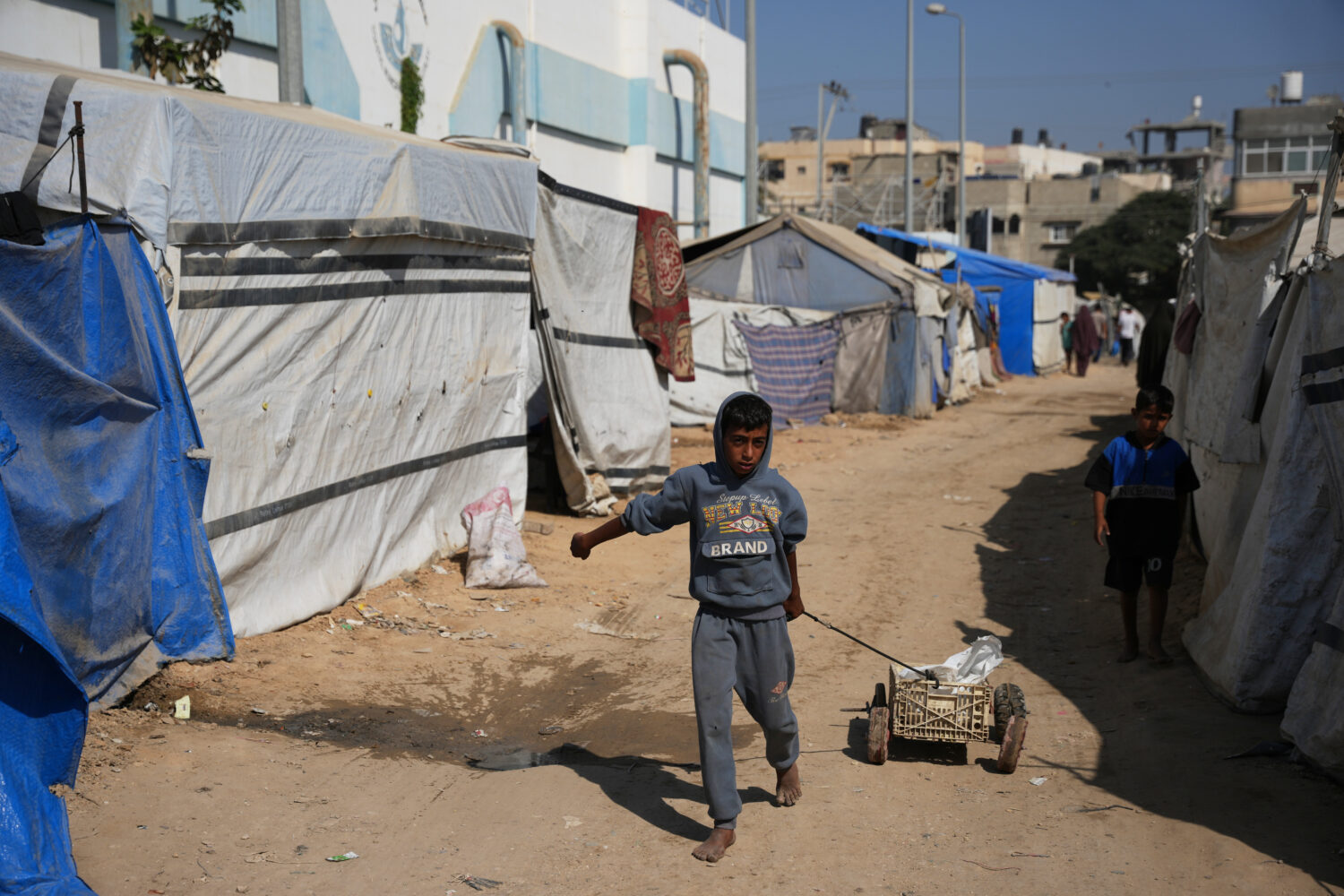 A Palestinian child pulls a cart between tents temporarily erected in a camp in Deir al‑Balah, ce...