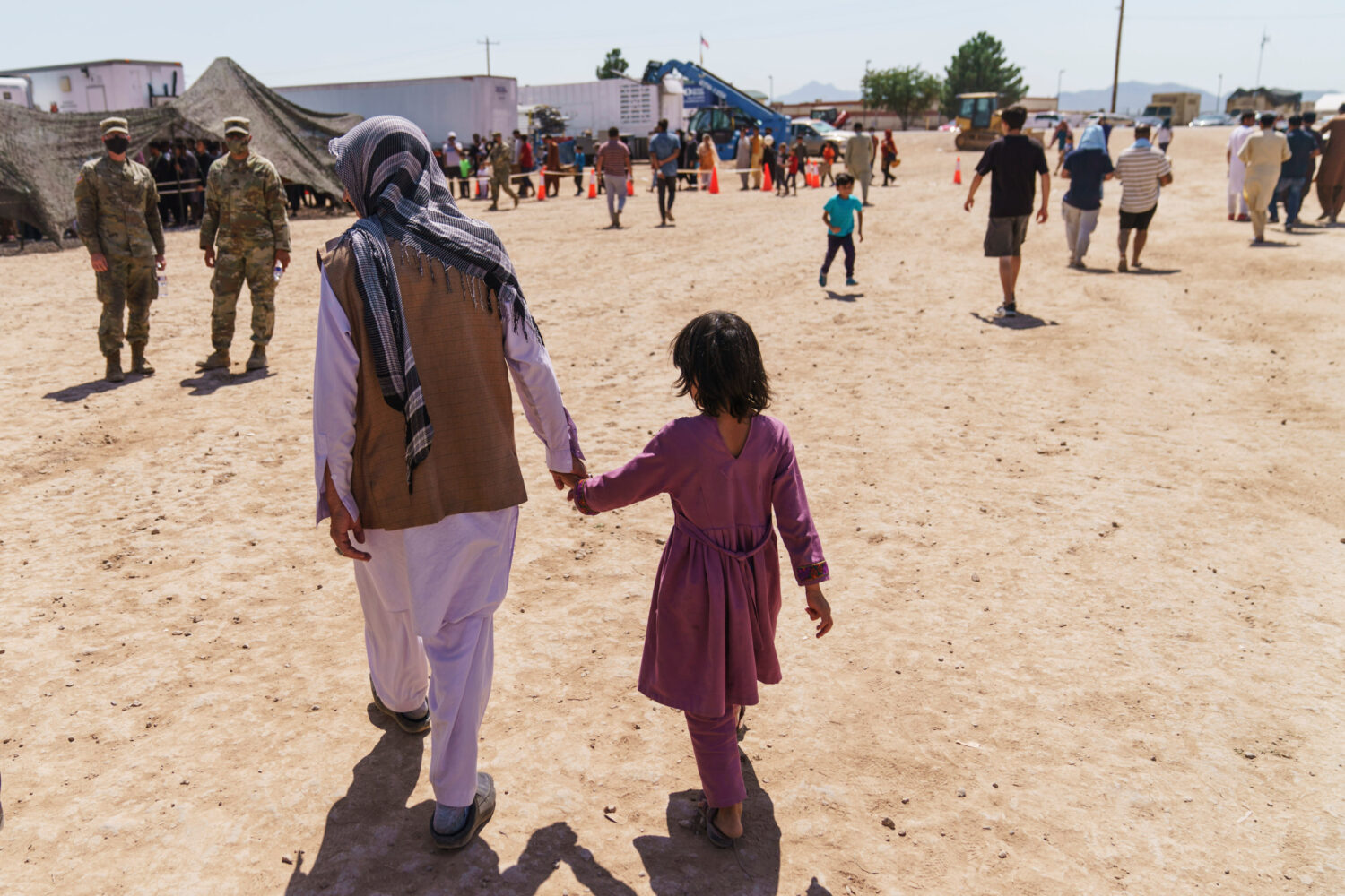 FILE - A man walks with a child through Fort Bliss' Doña Ana Village where Afghan refugees are bei...
