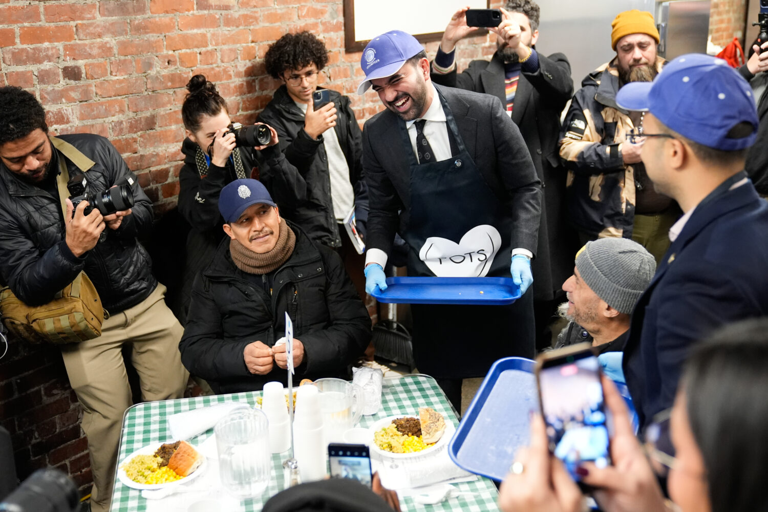 While surrounded by members of the media, New York City mayor-elect Zohran Mamdani, center, helps t...
