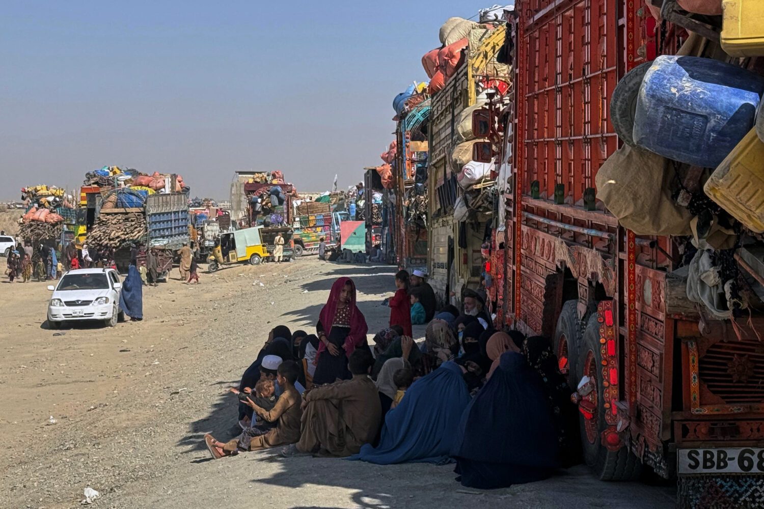 Afghan refugees sit beside trucks loaded with their belongings as they wait their turn to leave for...