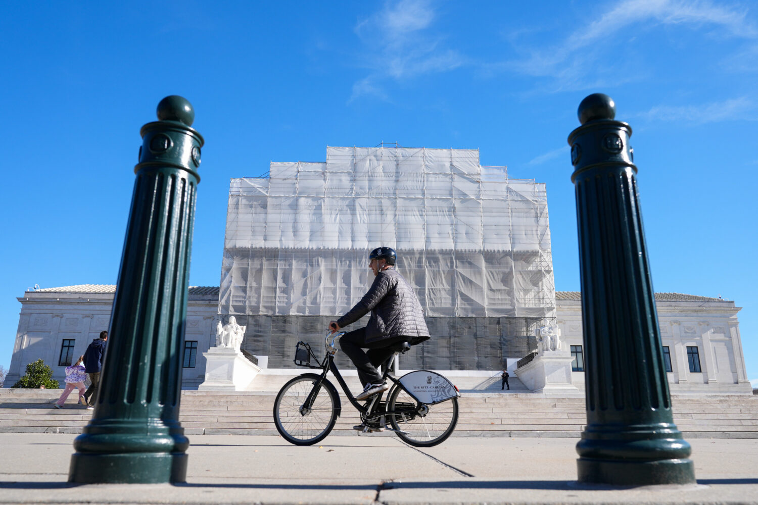 As a person on a bicycle rides past, construction on the front of the U.S. Supreme Court continues ...