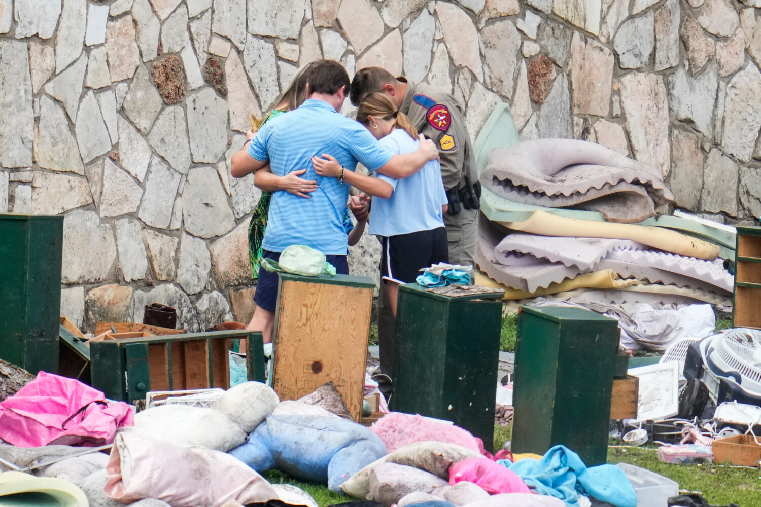 FILE - An officer prays with a family as they pick up items at Camp Mystic in Hunt, Texas, July 9, ...