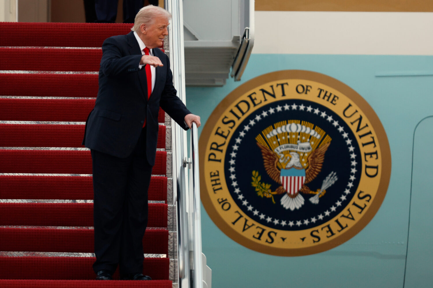 President Donald Trump gestures toward the media as he walks down the stairs of Air Force One upon ...