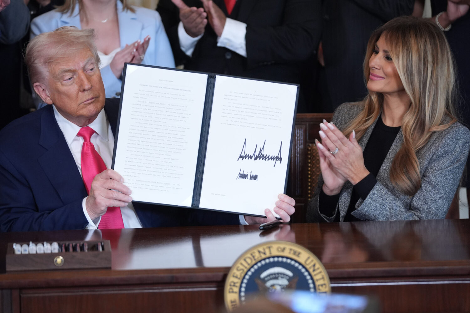President Donald Trump displays an signed executive order as first lady Melania Trump watches durin...