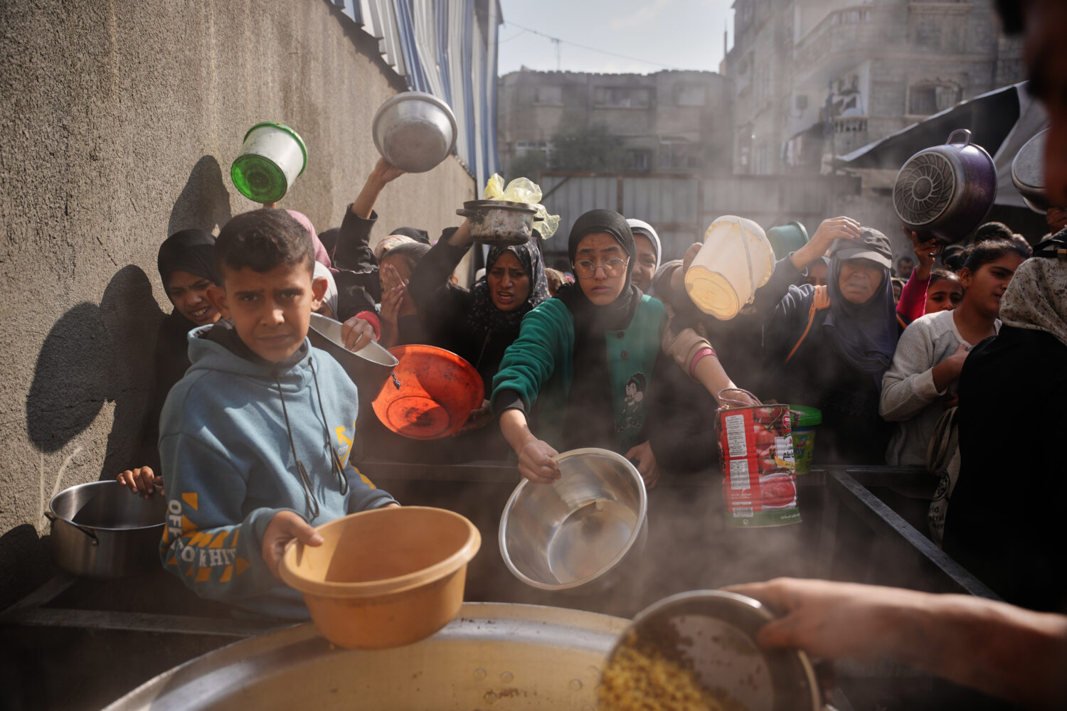 Palestinian women struggle to receive donated food at a community kitchen in Nuseirat, central Gaza...