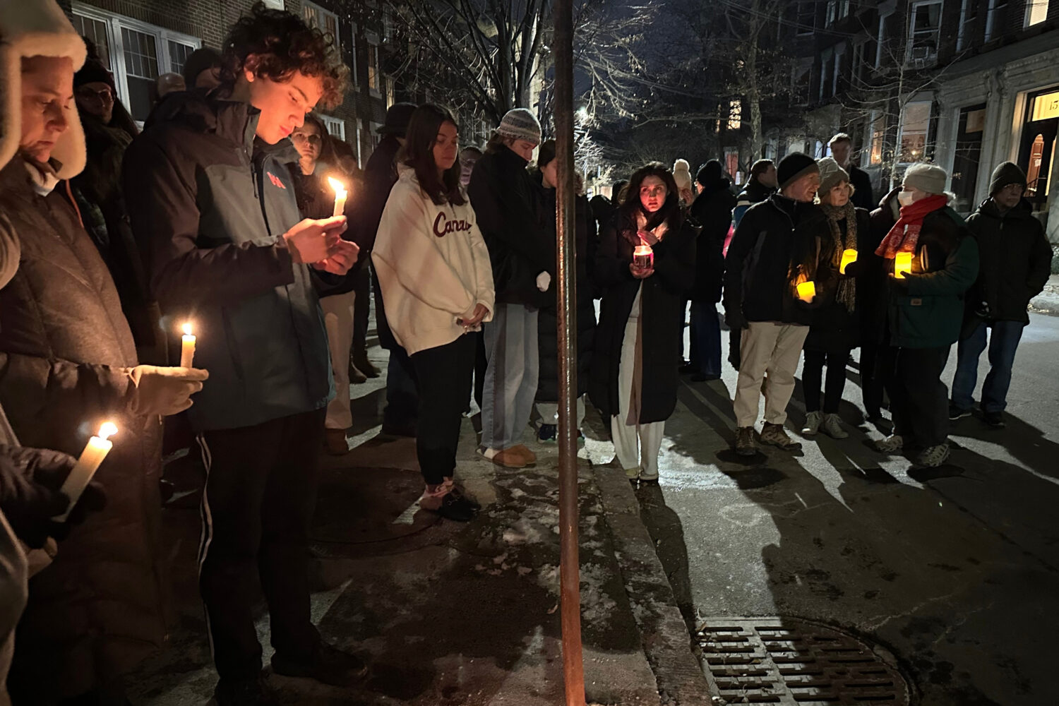 A crowd of people holding candles gather outside the home of Massachusetts Institute of Technology ...