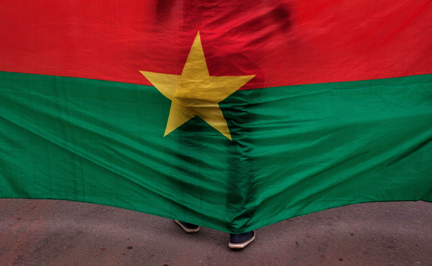 FILE - The Burkina Faso nationals flag with a man standing in front of it is seen during a memorial...