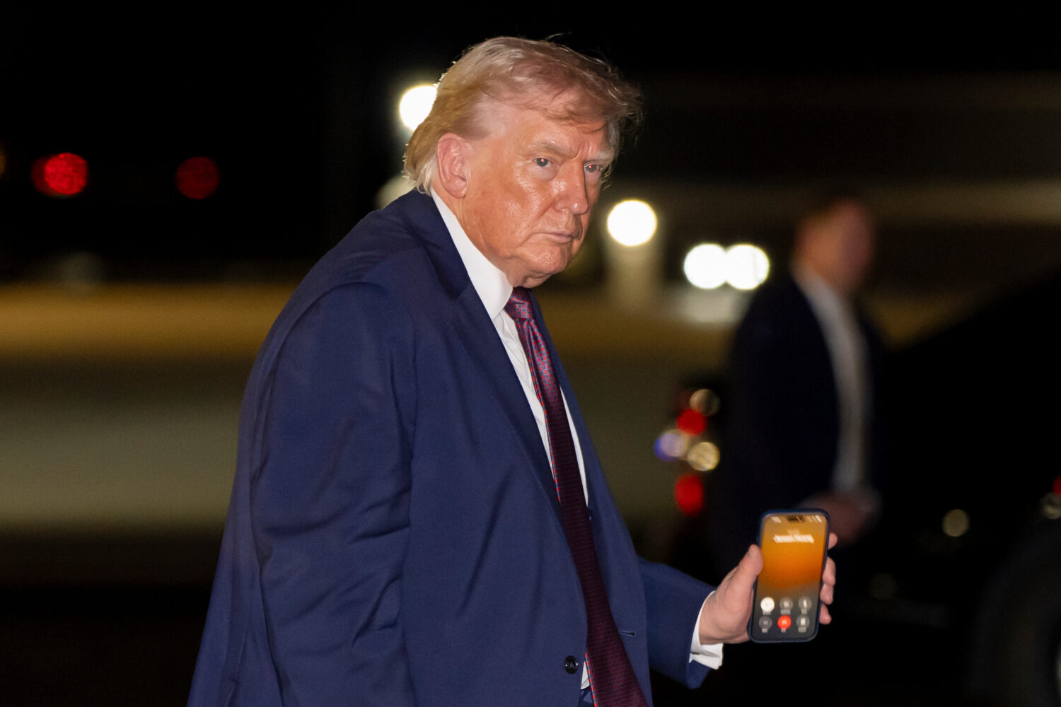 President Donald Trump holds a cell phone with a call to Nvidia CEO Jensen Huang as he departs on A...