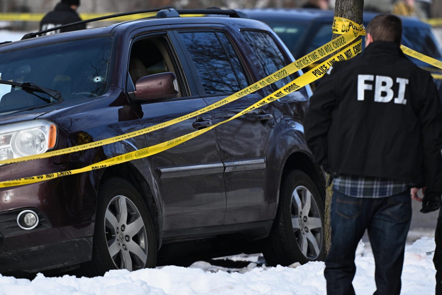A bullet hole is seen in the windshield as law enforcement officers work the scene of a shooting in...