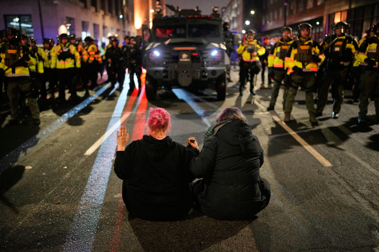 Two people sit in the street holding hands in front of Minnesota State Patrol during a protest and ...