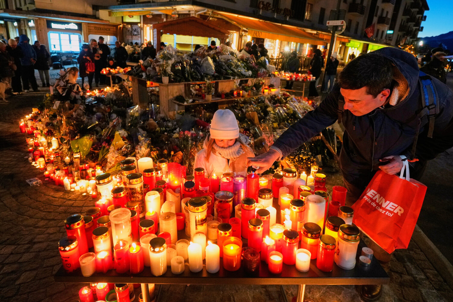 A child watches as an adult places a candle outside the sealed off Le Constellation bar in Crans-Mo...