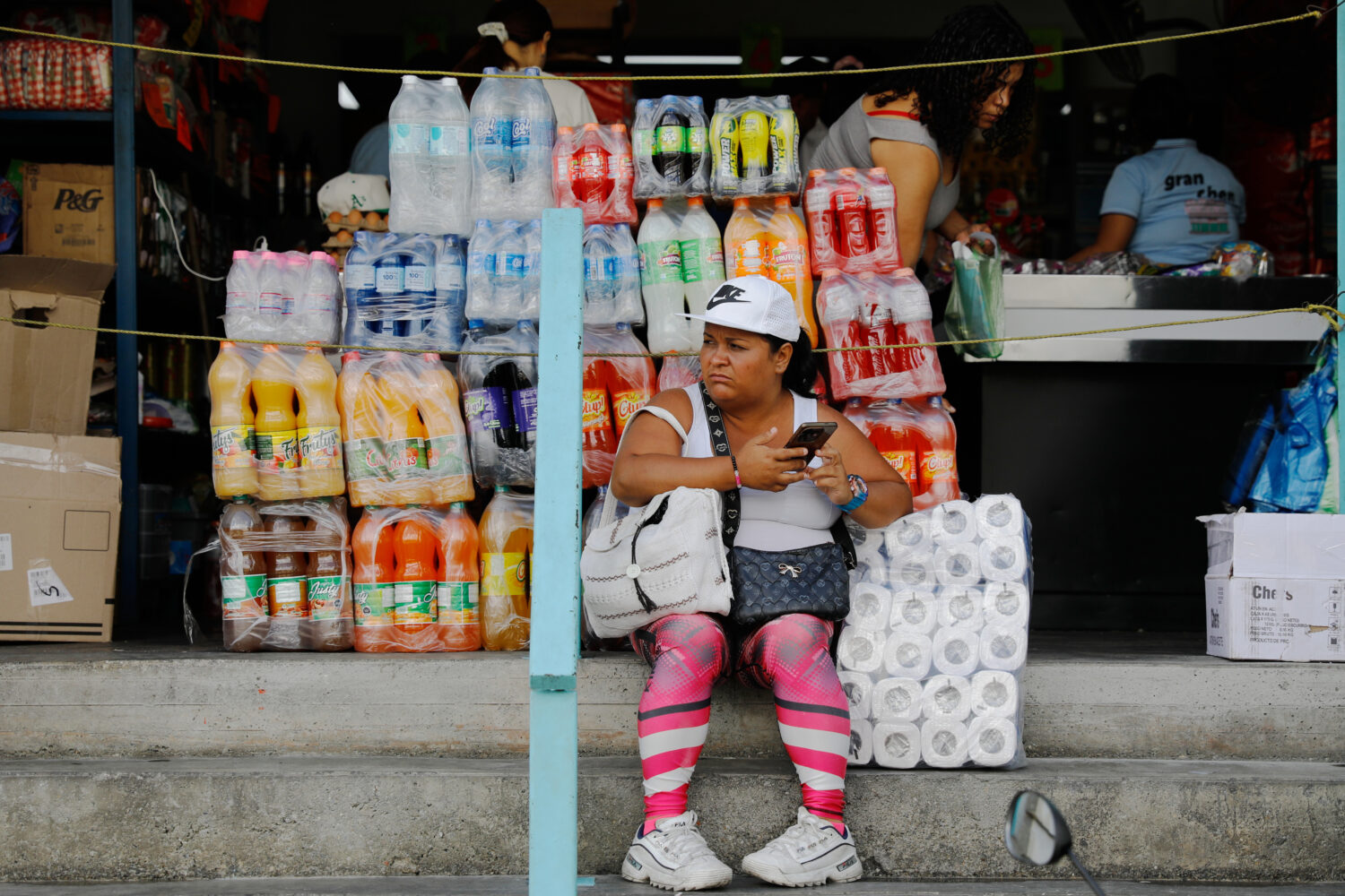 A woman sits in front of a store in the Petare neighborhood of Caracas, Venezuela, Wednesday, Jan. ...