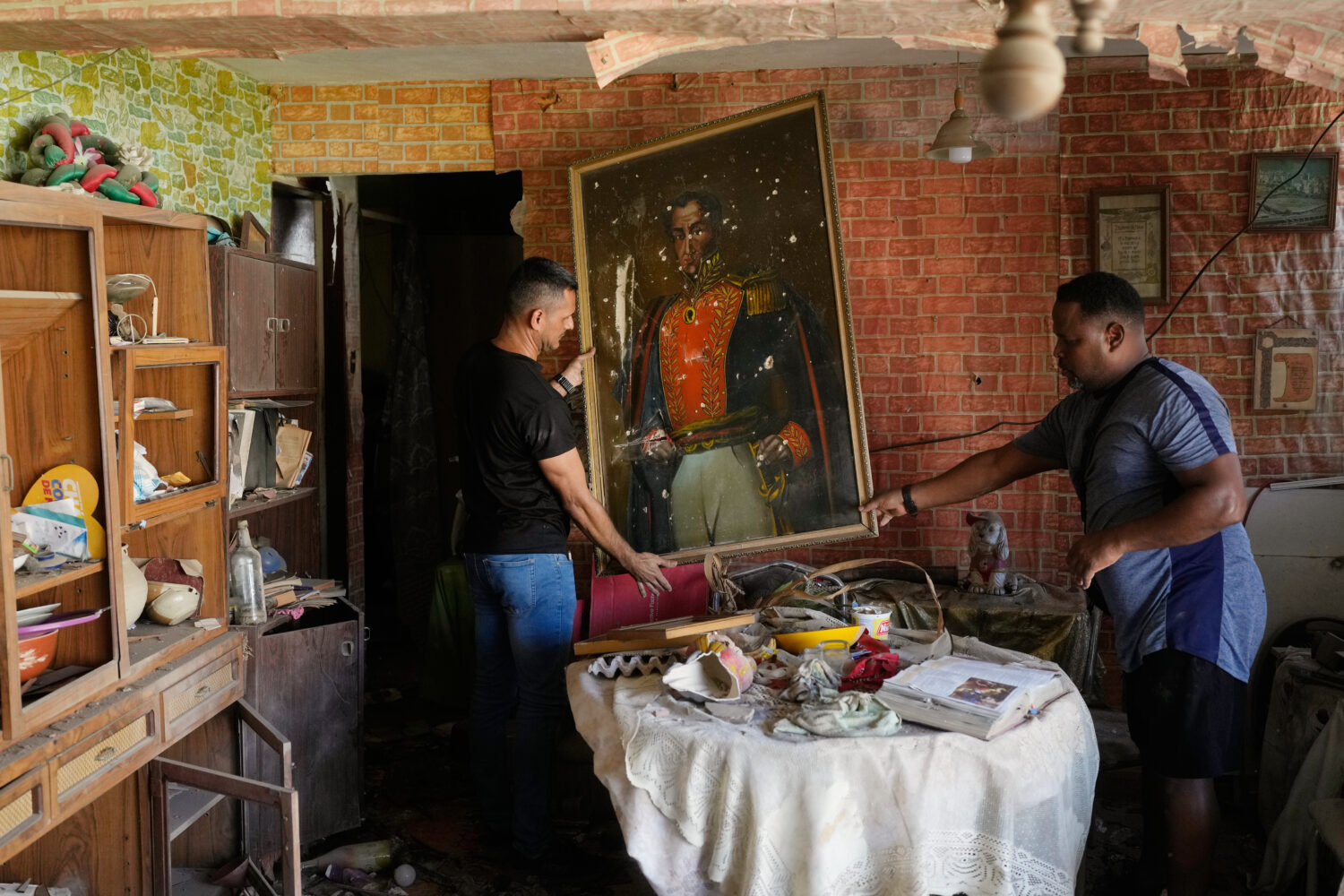Jesus Linares, right, removes a painting of independence hero Simon Bolivar at his home, which he s...