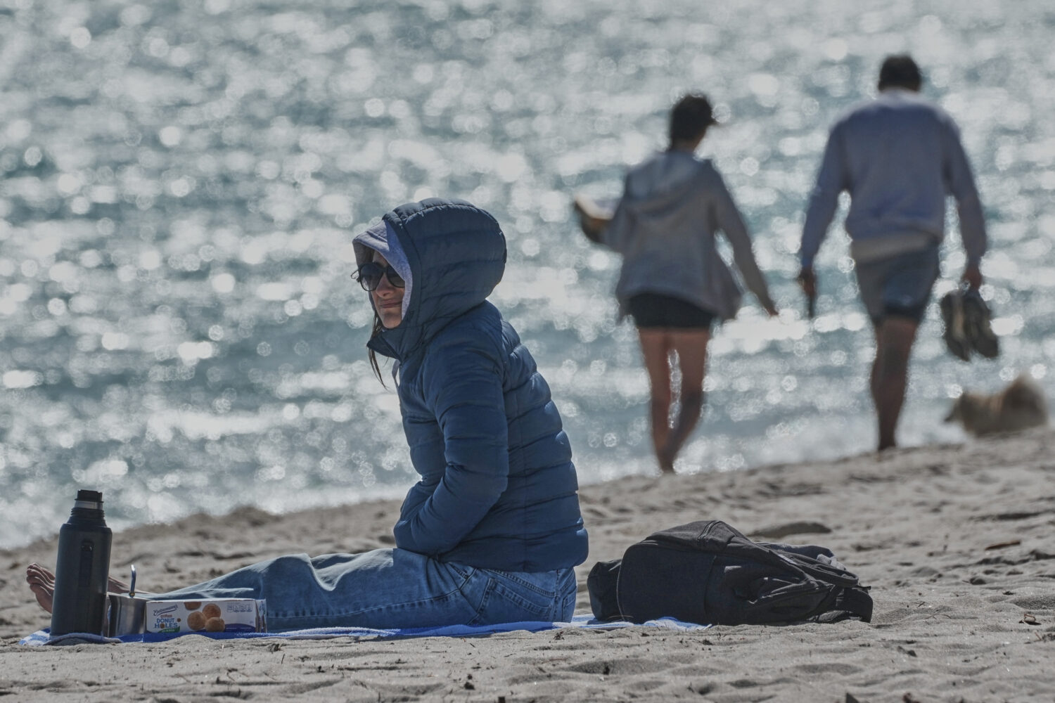 A bundled up Lucia Amato, of Argentina, sits on the shore while waiting for a friend in Miami Beach...