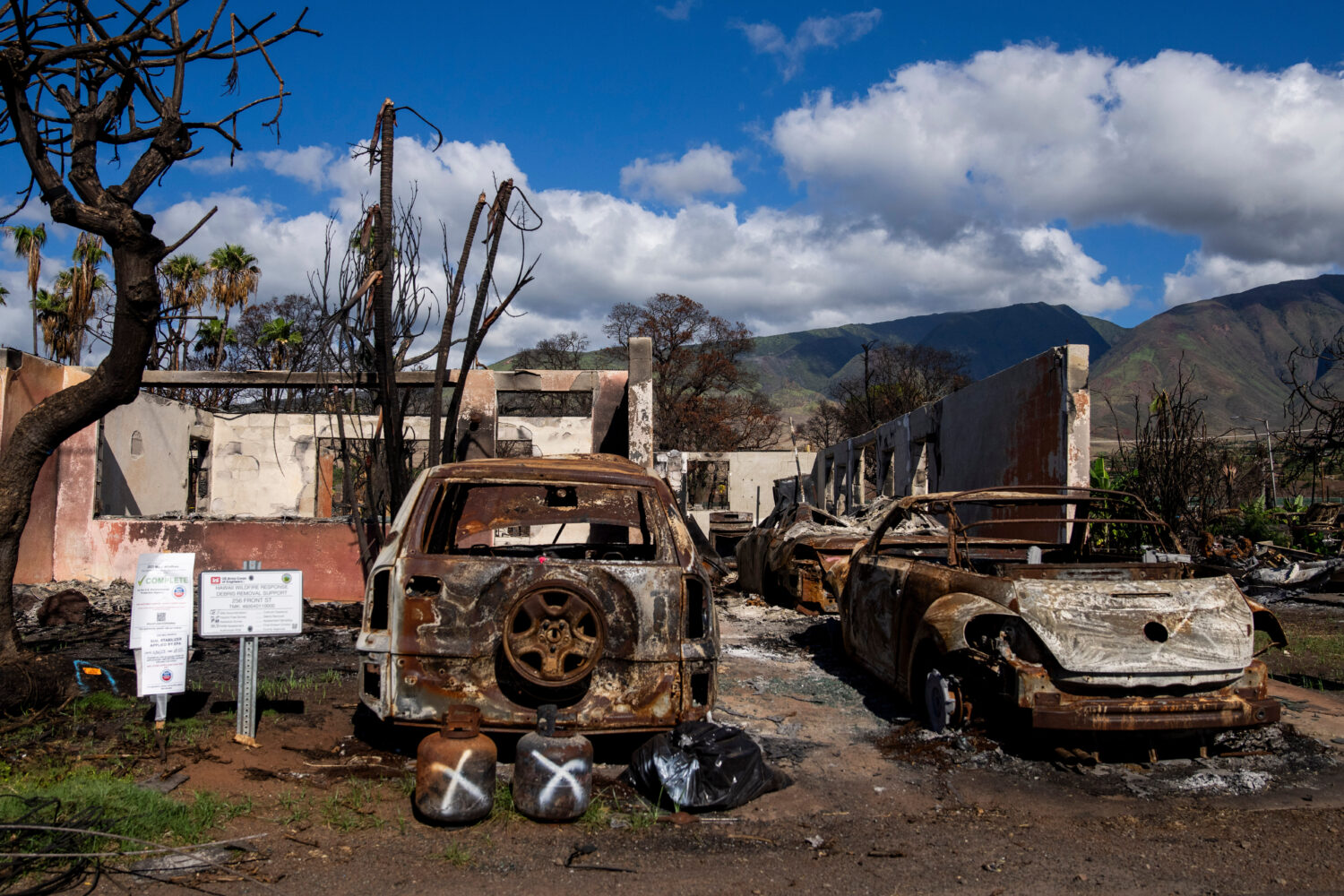 FILE - Burned cars and propane tanks with markings on them sit outside a house destroyed by wildfir...