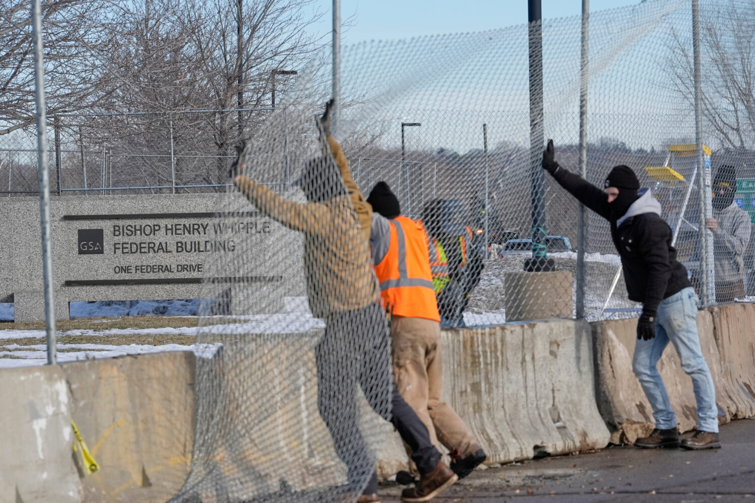 Masked workers put up fencing around the Bishop Whipple Federal Building, Monday, Jan. 12, 2026, in...
