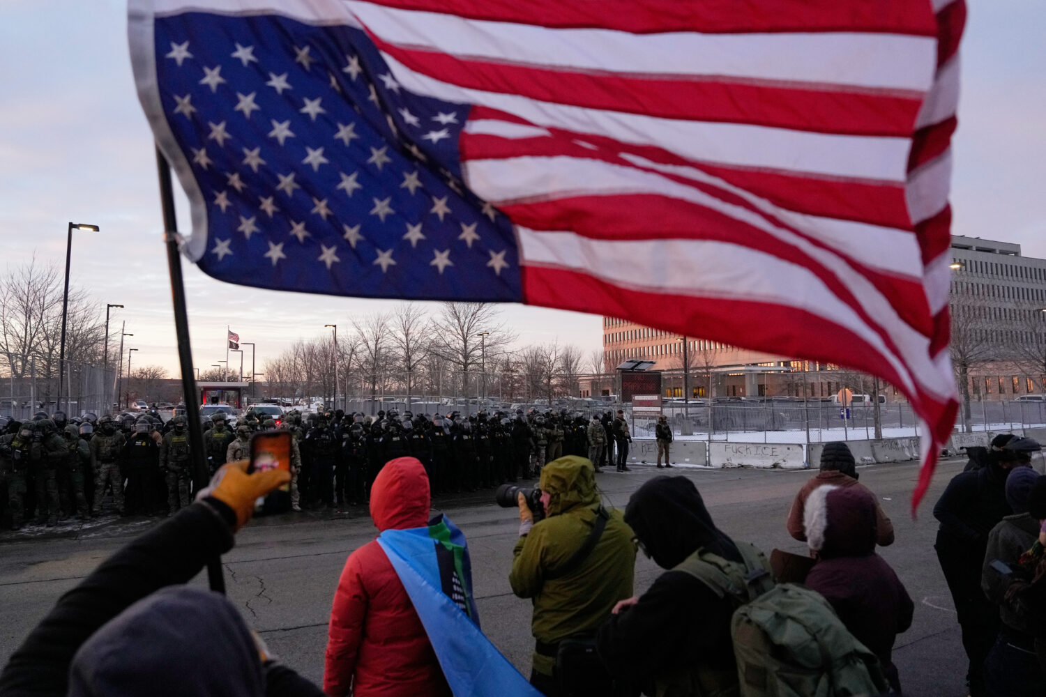 A person holds an upside-down American flag as law enforcement stand during a protest outside the B...