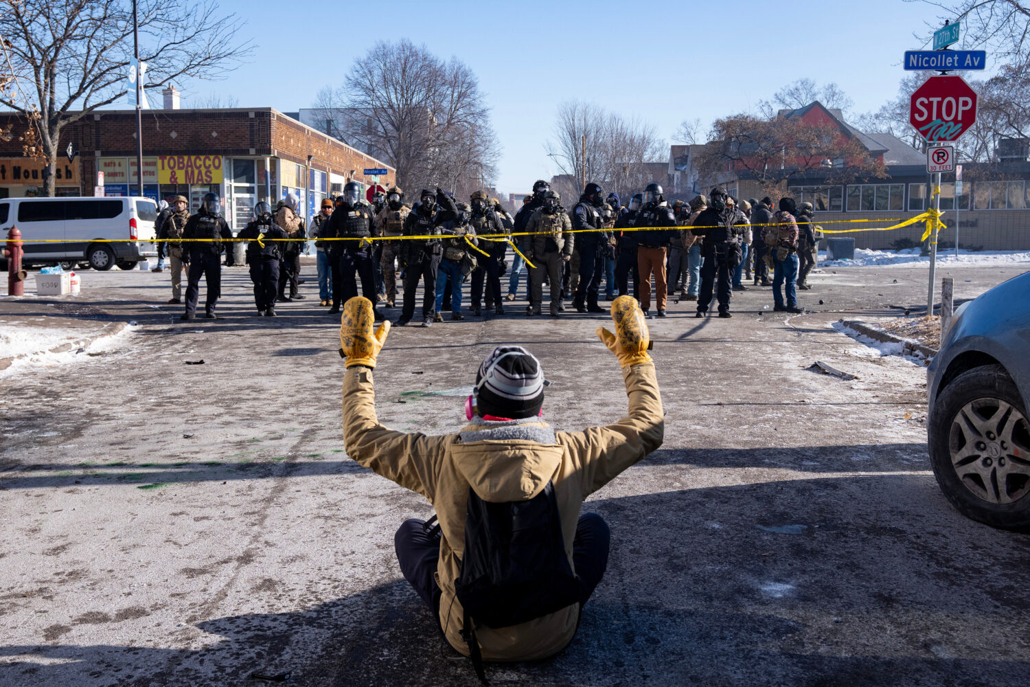 A protester sits on the street with his arms up in front of federal agents in Minneapolis, on Satur...