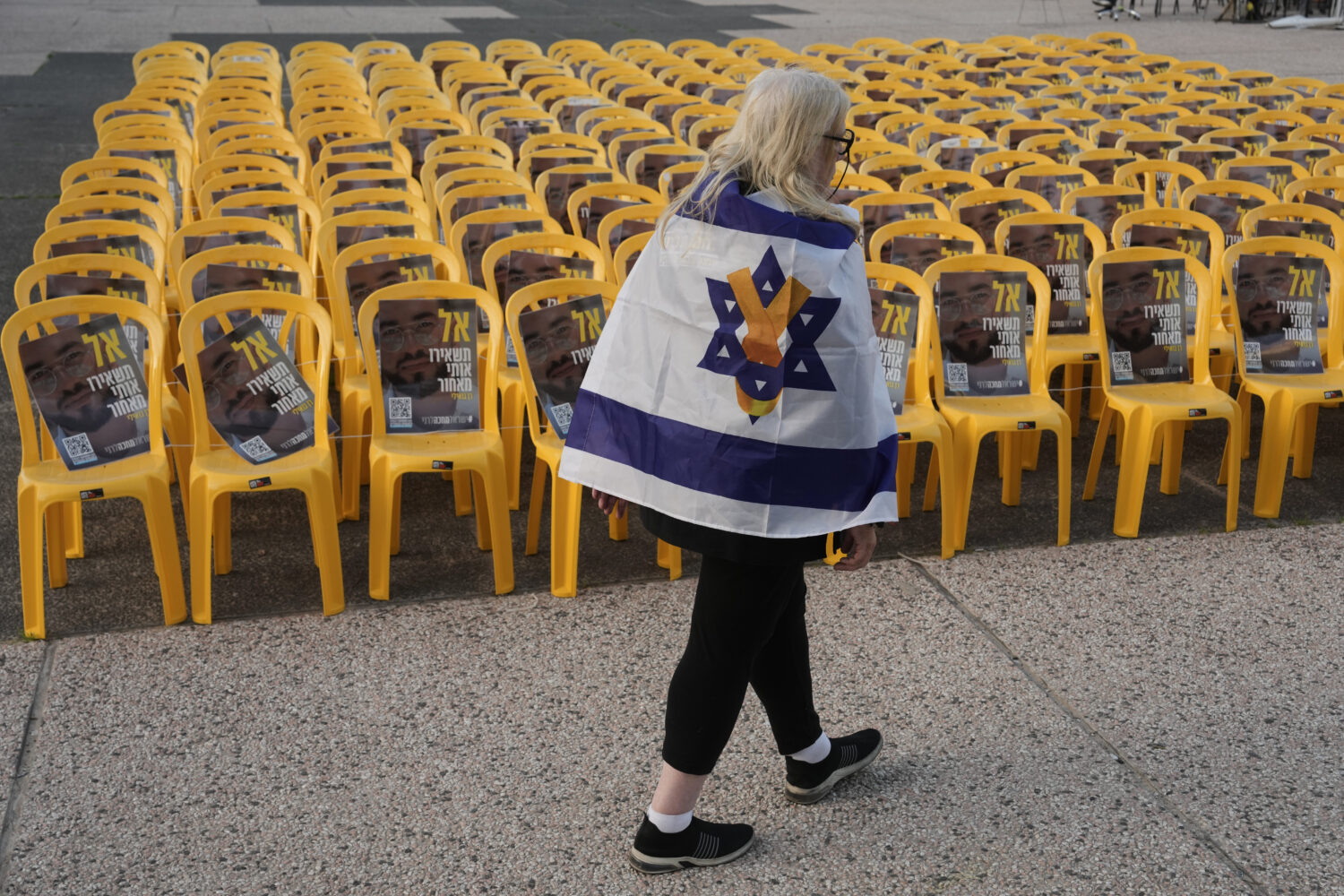A woman walks by chairs with photo of Ran Gvili, the final hostage in Gaza who was killed while fig...