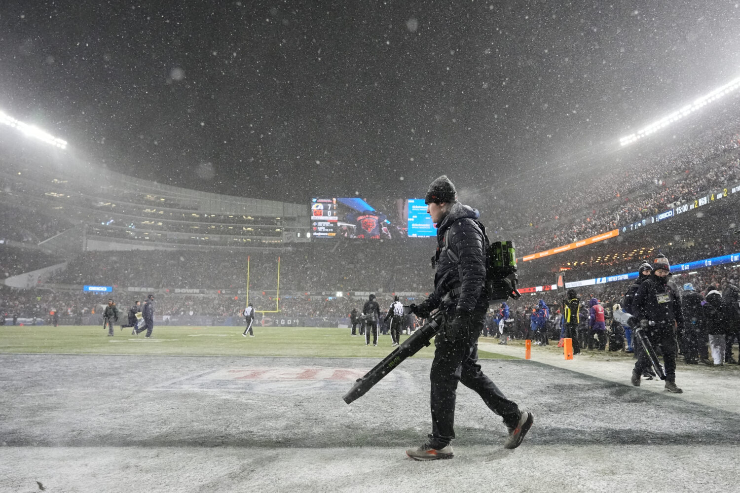 Grounds crew members glow snow off the field at Soldier Field during the first half of an NFL footb...