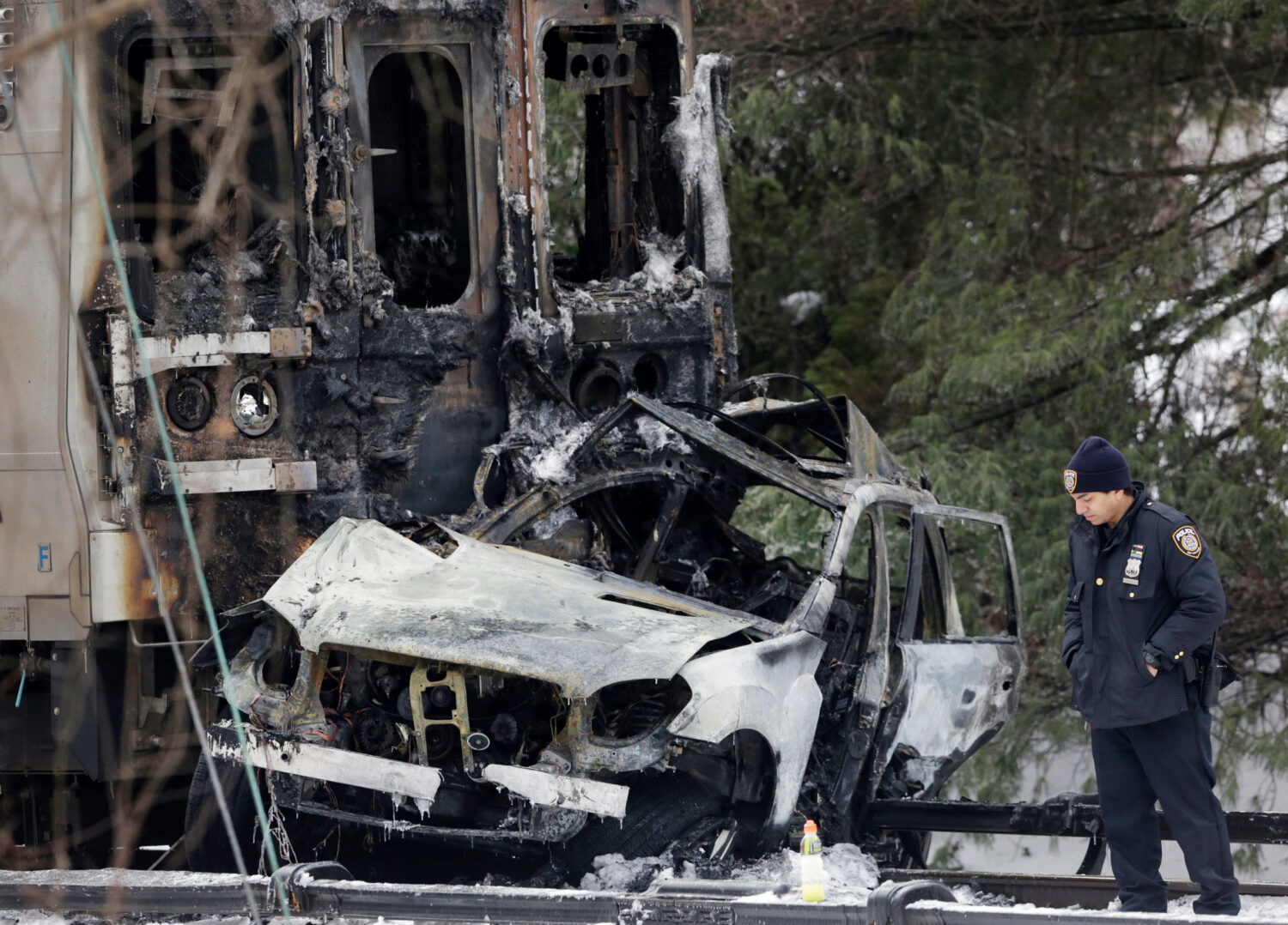 FILE - A police officer looks at an SUV that was crushed at the front of a Metro-North Railroad tra...