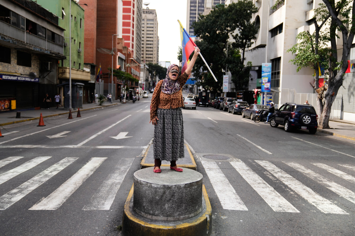 A supporter of Venezuelan President Nicolas Maduro stands on a median strip waving a national flag ...