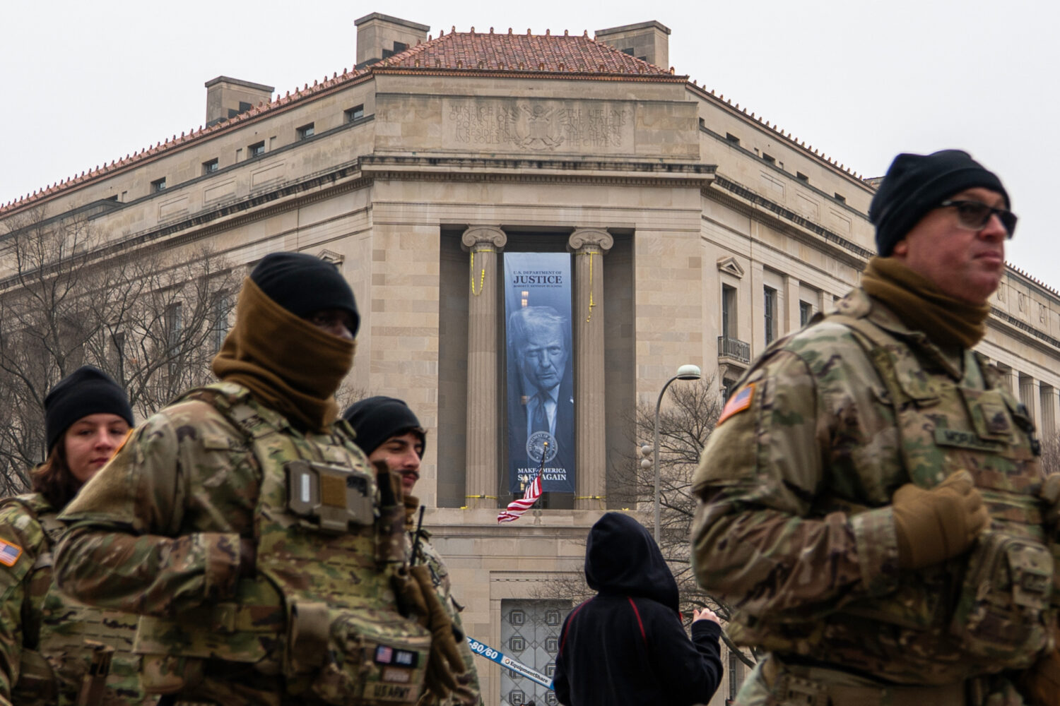 Members of the National Guard walk past a banner with President Donald Trump hanging on the Departm...