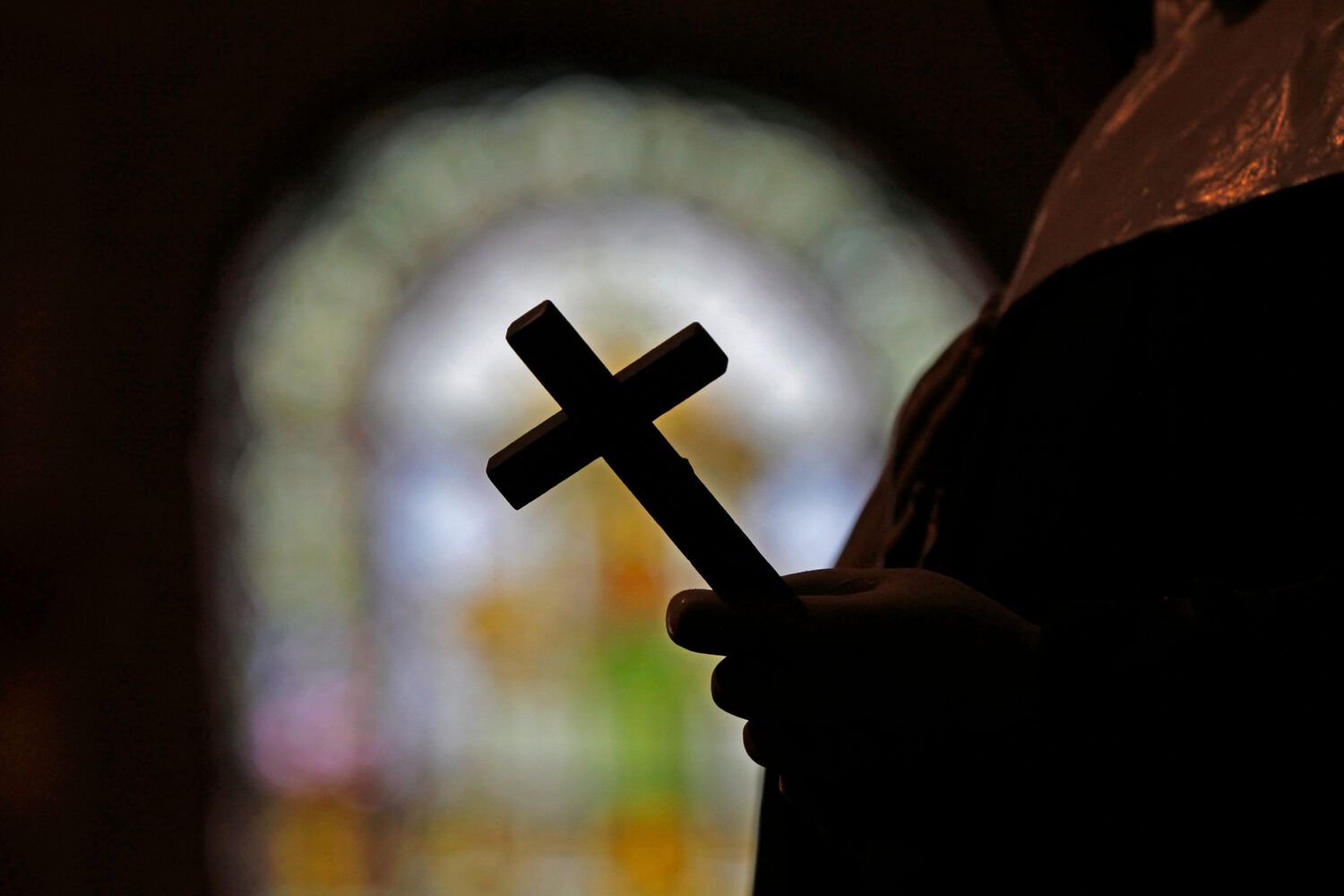 FILE - A cross is silhouetted against a stained glass window inside a Catholic Church in New Orlean...