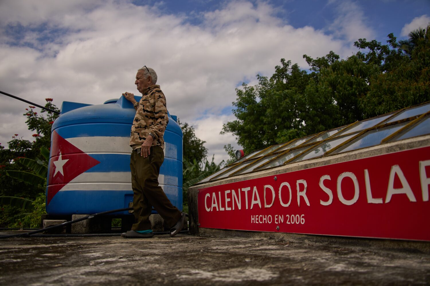 Felix Jose Morfi stands by his solar-powered water heater system he set up on his home's roof in Re...