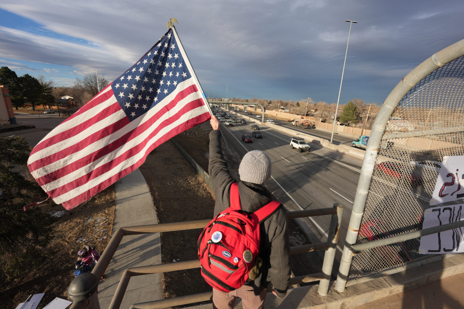 A protester holds American flag while waving at motorists Wednesday, Jan. 28, 2026, from an overpas...
