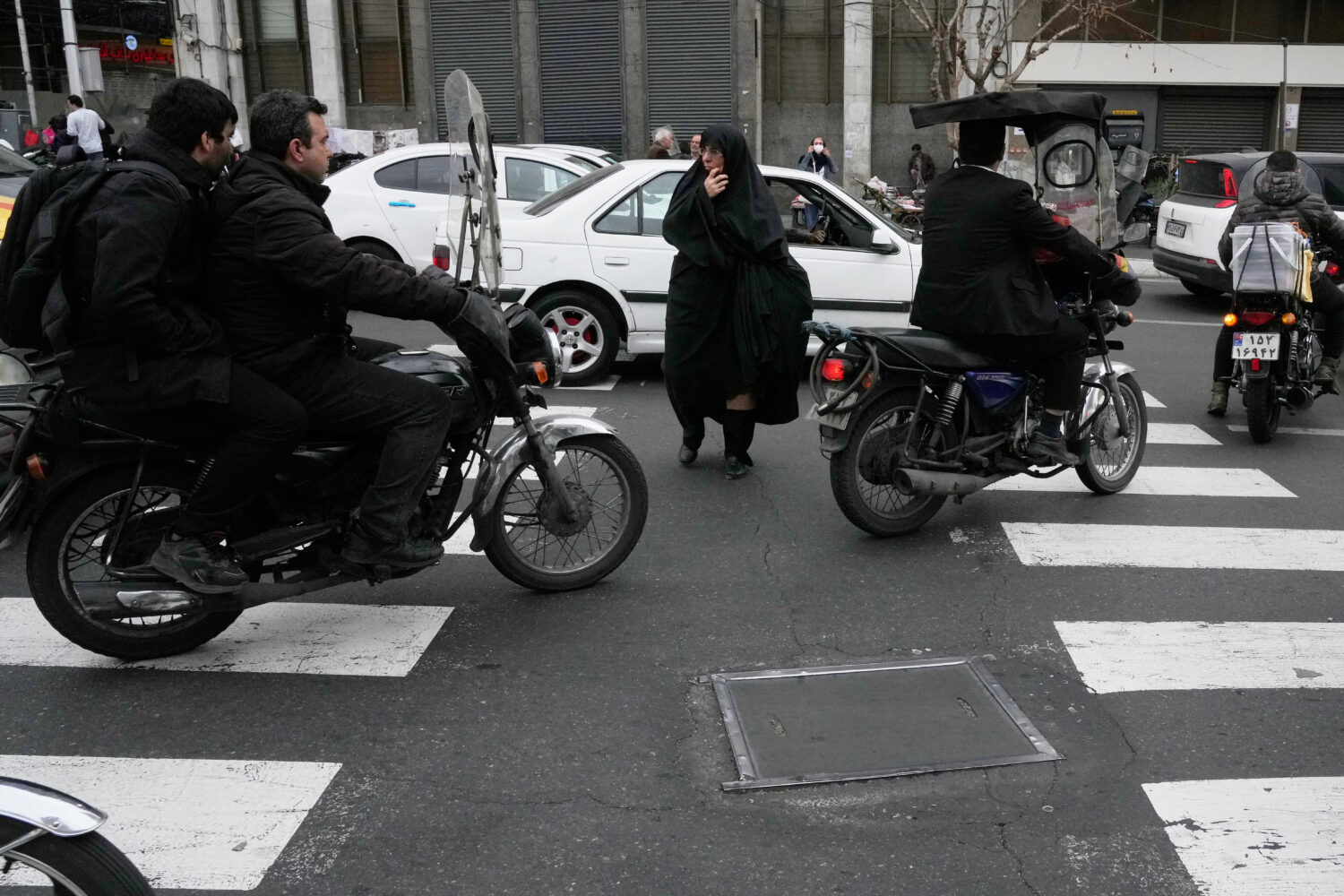 A woman crosses a square as motorbikes ride past in downtown Tehran, Iran, Tuesday, Feb. 24, 2026. ...