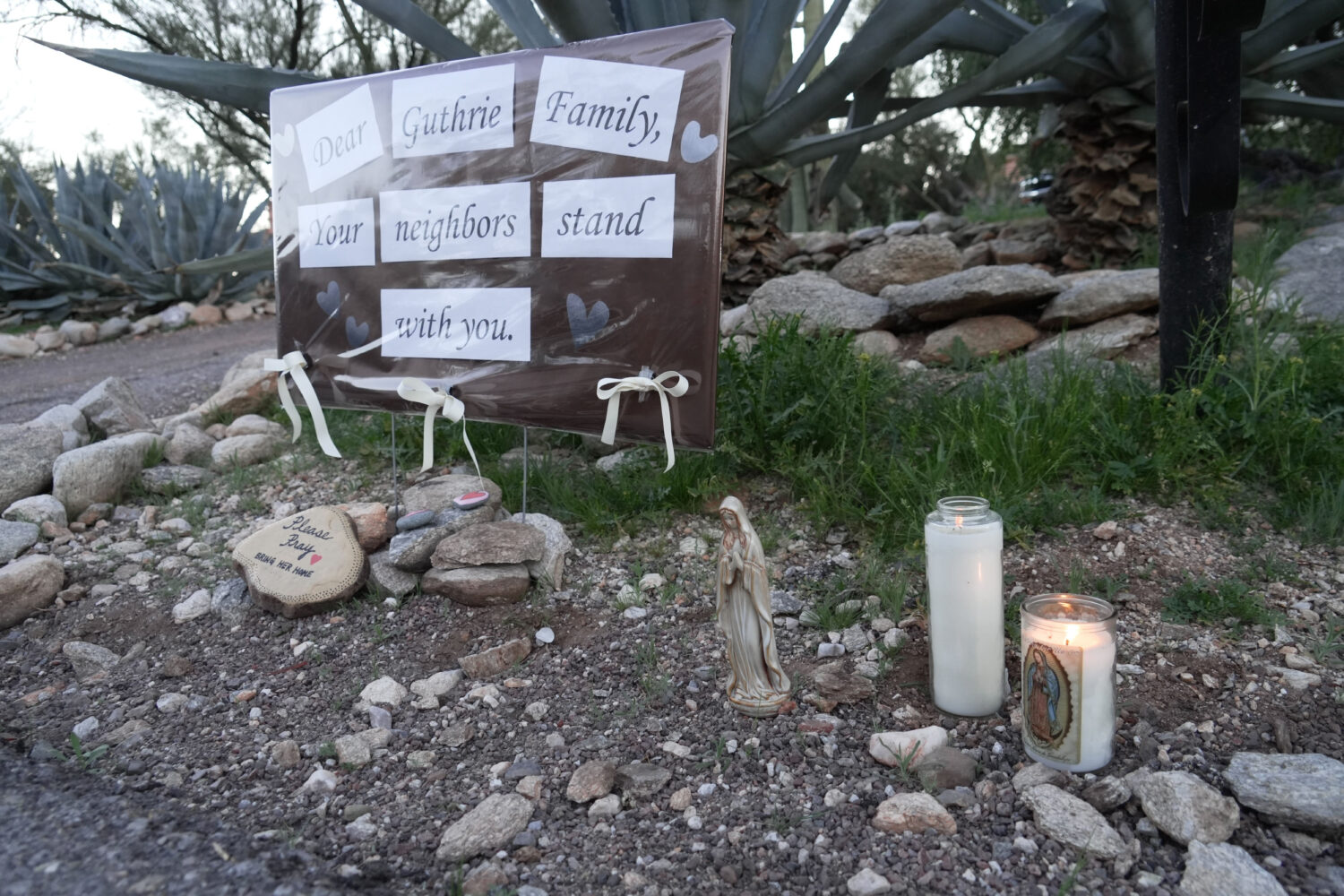 Lit candles next to a sign from neighbors supporting the Guthrie family outside of Nancy Guthrie’...