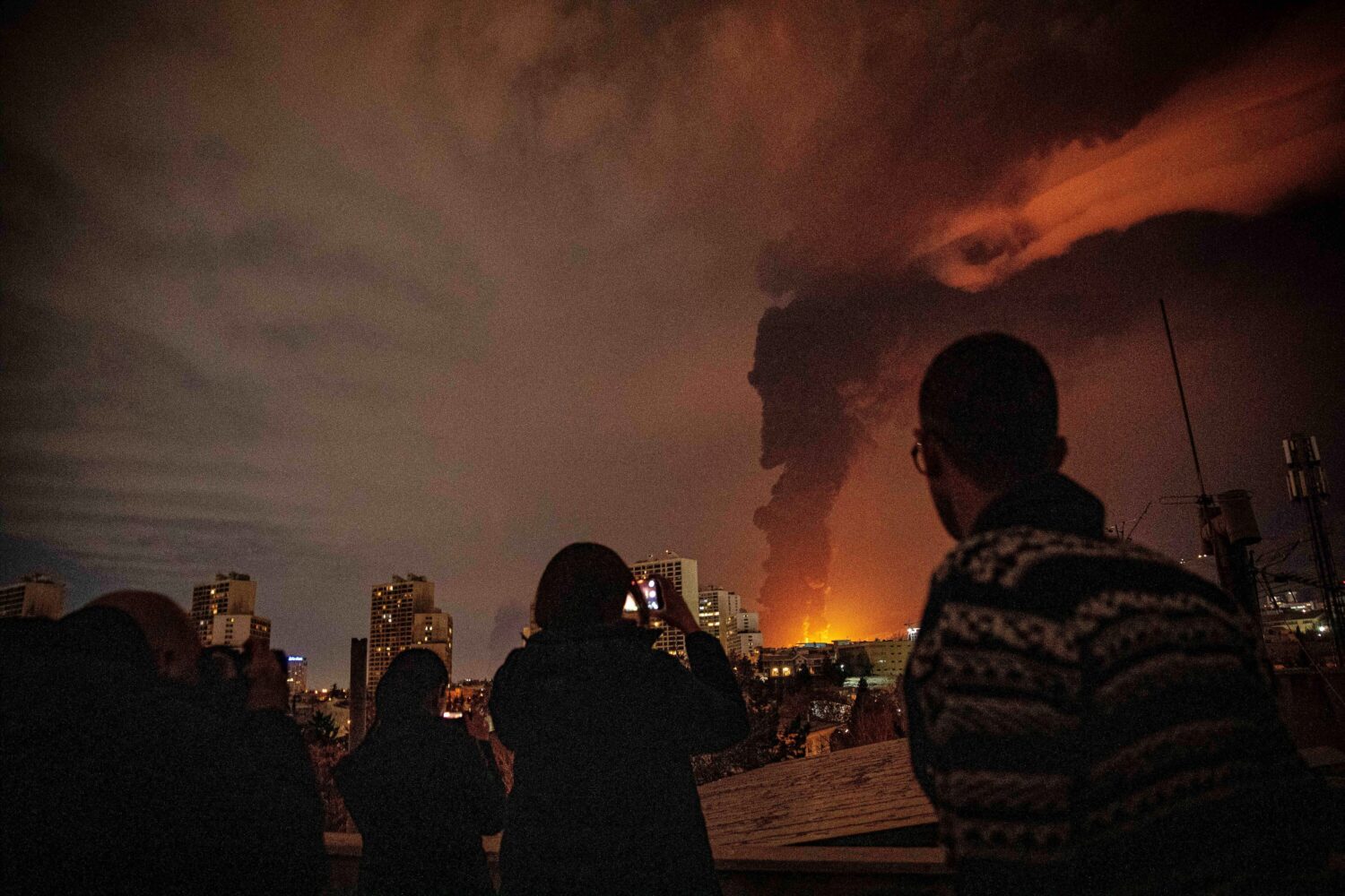Residents watch and take pictures as flames and smoke rise from an oil storage facility struck as a...