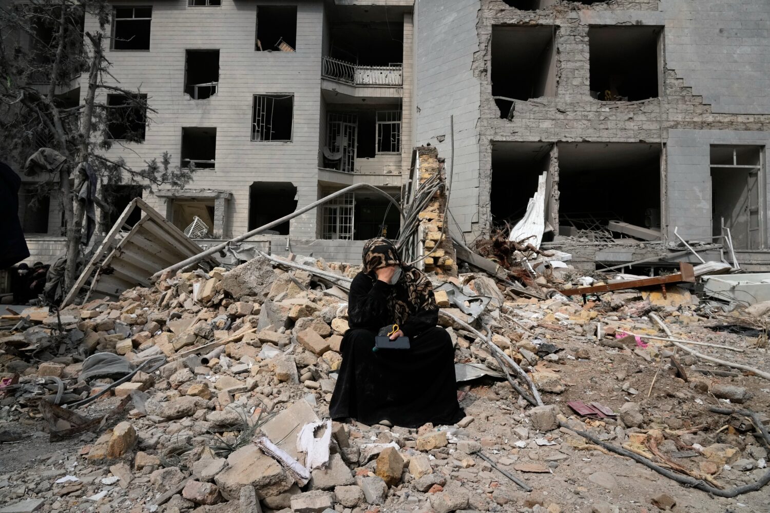 A woman sits on rubble across from a residential building damaged last Sunday during the U.S.-Israe...