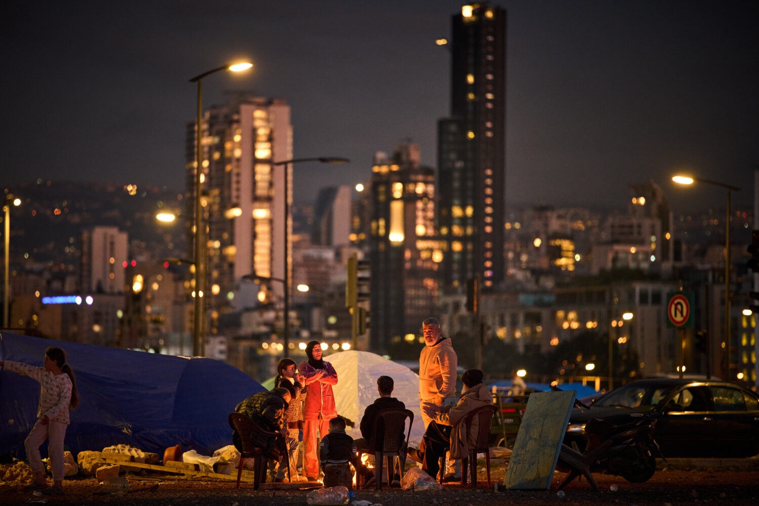 A family who fled Israeli shelling in southern Lebanon warm themselves by a bonfire next to tents u...