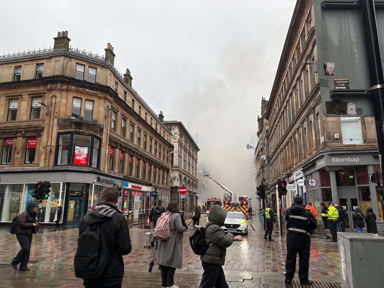 People look at smoke rising as firefighters damp down the remains of a fire which broke out in a bu...