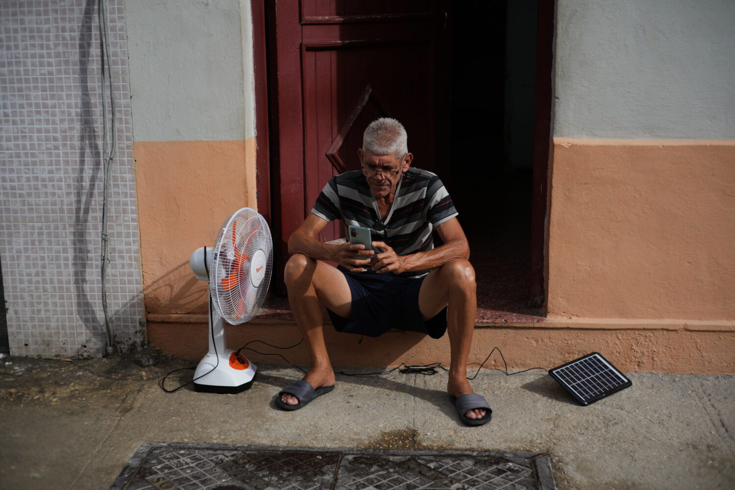 A man charges his phone and his fan with a solar panel during a blackout in Havana, Tuesday, March ...